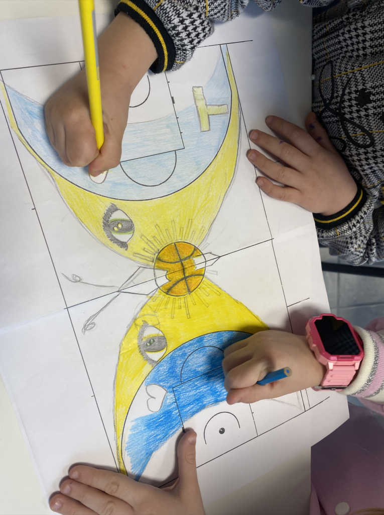IMMAGINE: Due bambine colorano con matite gialle e blu il disegno progettuale di un campo da basket, decorato con forme curve, occhi stilizzati e un pallone al centro.