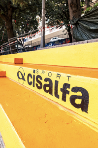 Primo piano delle gradinate del campo da basket ai Giardini Buonvicini, dipinte di giallo e arancione con il logo nero di Cisalfa Sport, partner del progetto.